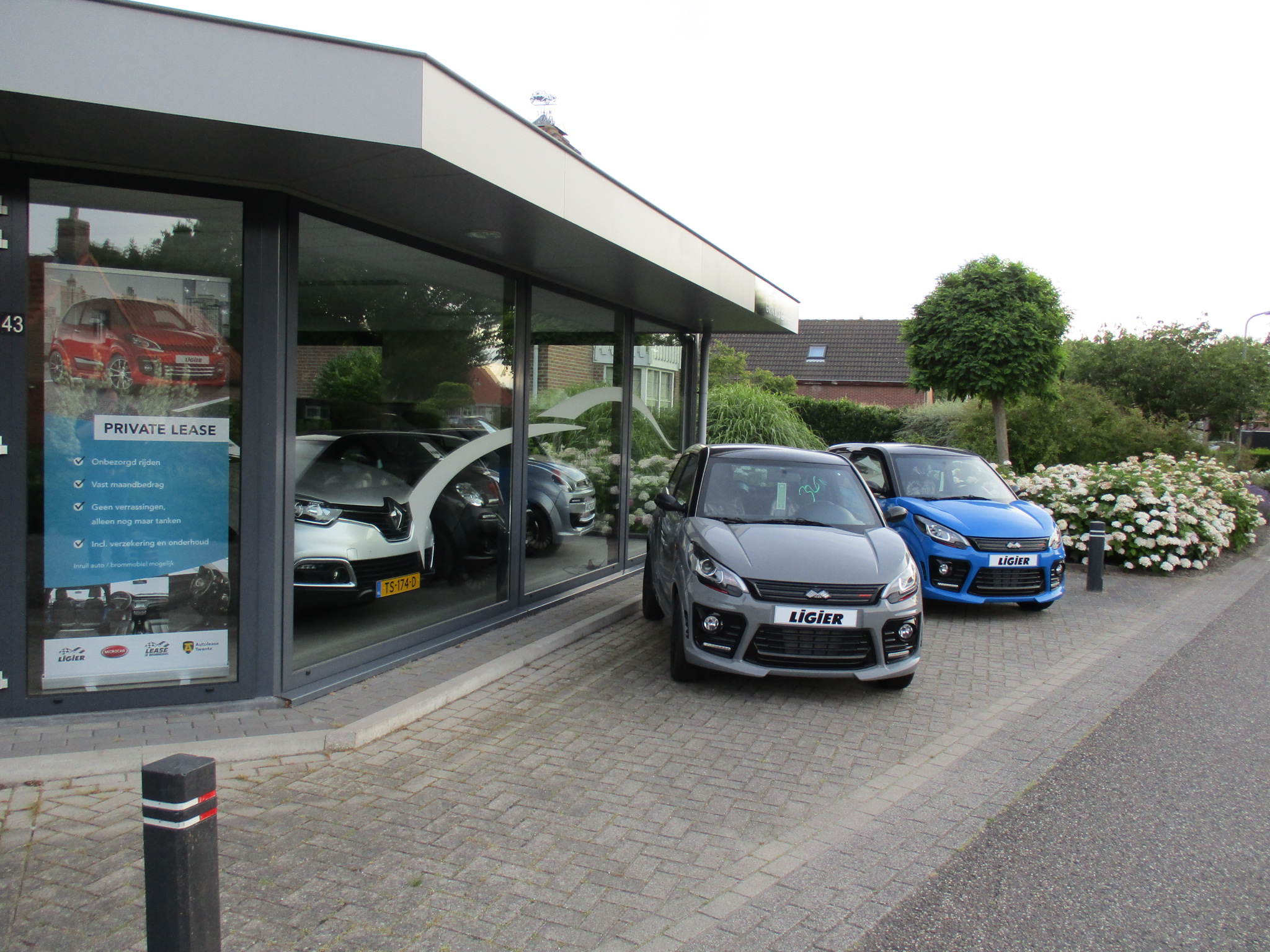 Twee Ligier brommobielen, een grijze en een blauwe, voor de showroom van Garage Grinwis